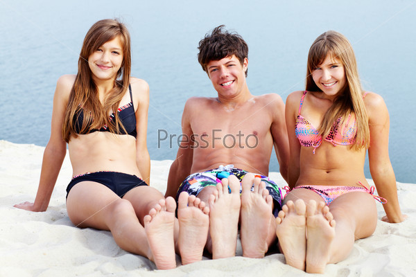 Young people sitting on sand and tanning on a sunny summer day