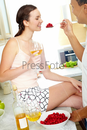 Image of happy woman with glass of wine looking at spoonful of raspberries in her husband hand