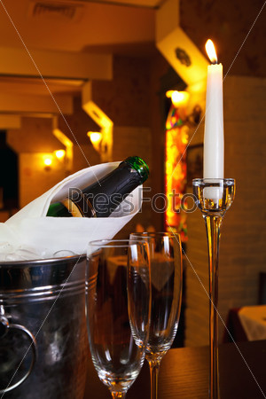 glasses of champagne and a bucket with a candle and a rose on the background of the restaurant