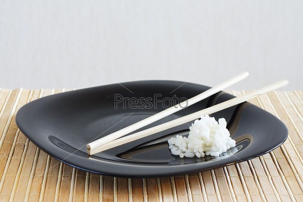 Black dish with white rise on a bamboo table cloth still life