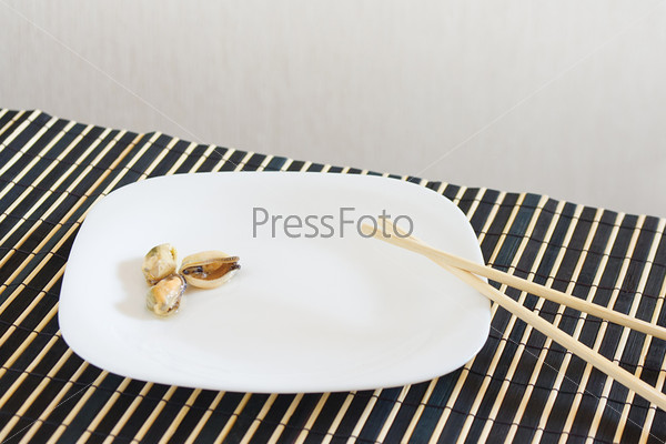 White dish with mussels and chopsticks on a bamboo table cloth still life
