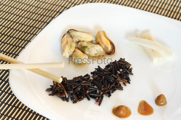 White dish with black rise, mussels and squid on a bamboo table cloth still life