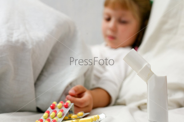 An ill girl on a bed under cover. Pills with mixsture closeup.