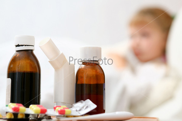 An ill girl on a bed under cover. Pills with mixture closeup.