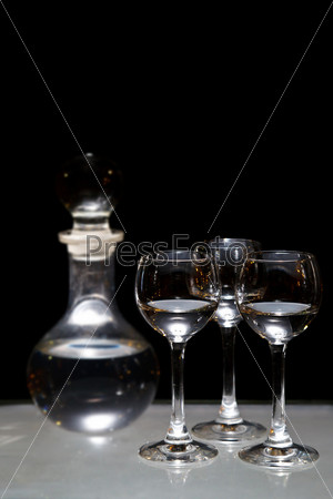 Три рюмки водки и бутылка на столе на черном фоне