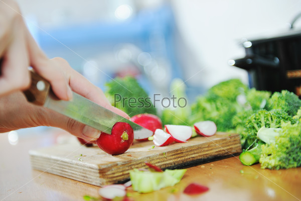 Женщина режет ножом зеленые и красные овощи для полезного салата
