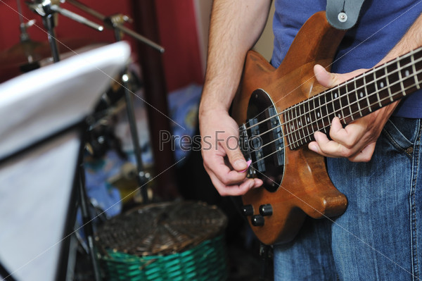 Молодой бас-гитарист играет на домашней гаражной репетиции с группой друзей