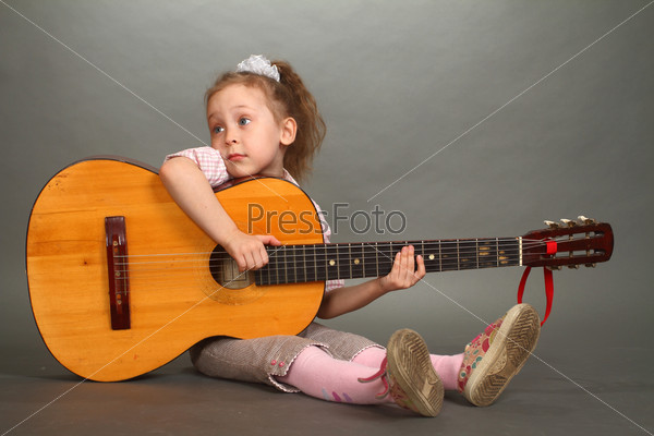the little girl sits on a floor with a big guitar, a look not in a lens, a double 2