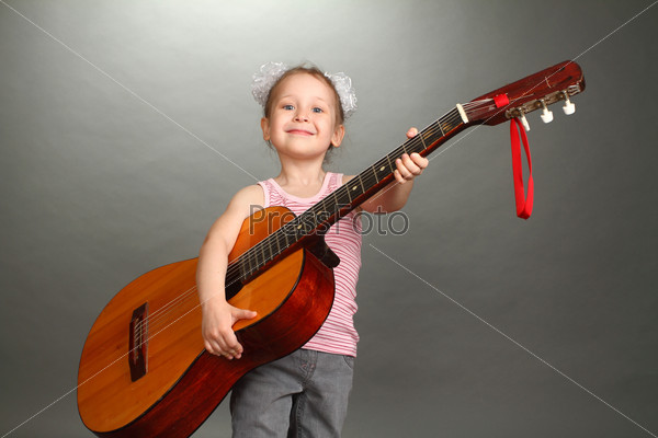 the little girl costs with a big guitar in hands, a look not in a lens, smiles, a double 4