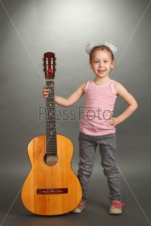the little girl costs with a big guitar, a look not in a lens, smiles, a guitar holds for a signature stamp, a vertical shot, a double 3