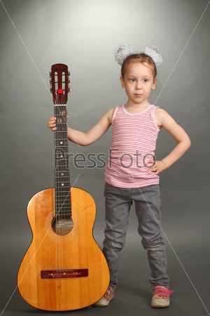 the little girl costs with a big guitar, a look not in a\
lens, smiles, a guitar holds for a signature stamp, a vertical\
shot, a double 2