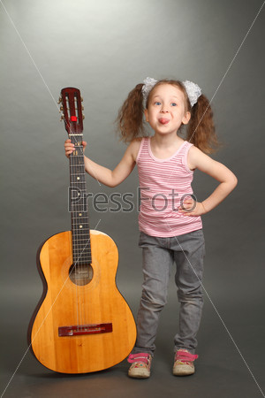 the little girl costs with a big guitar, a look not in a lens, puts out the tongue, a guitar holds for a signature stamp, a vertical shot,