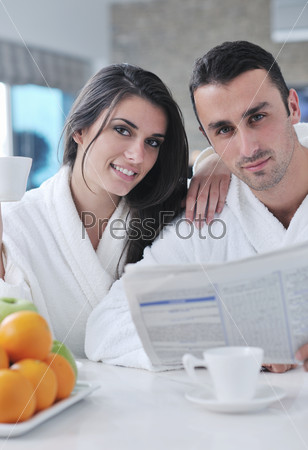 Happy couple reading the newspaper in the kitchen at breakfast