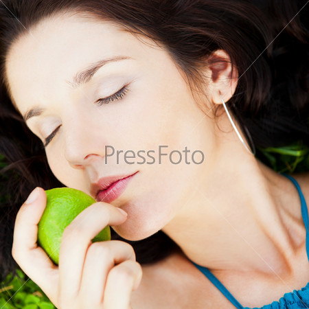Pretty brunette girl wearing elegant dress relaxing outdoor in green grass and smells aromatic lemon or lime citrus