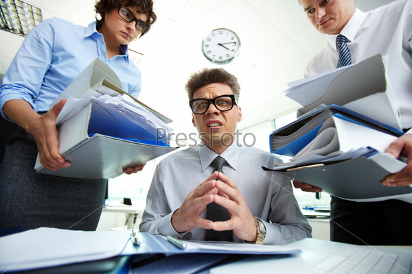 Terrified accountant looking at camera being surrounded by his partners holding huge piles of documents