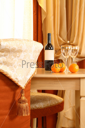 table fragment, on it a bottle of wine and two glasses, in the foreground a chair back