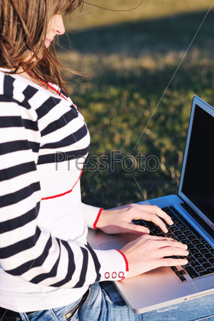 young teen woman work on laptop computer outdoor in nature with blue sky and green grass in background