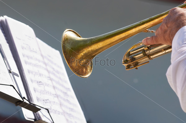 The hand of the musician plays on trumpet opposite to a lectern with notes