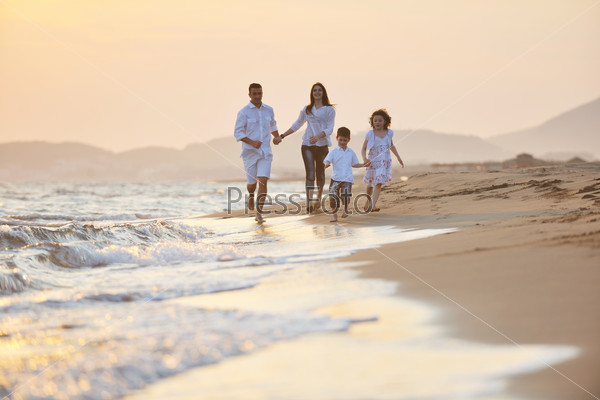 Счастливая семья, бегущая по морскому пляжу на закате солнца