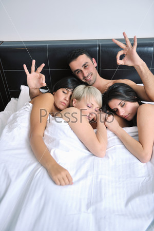 Young handsome man lying in bed with three girls - Stock Image