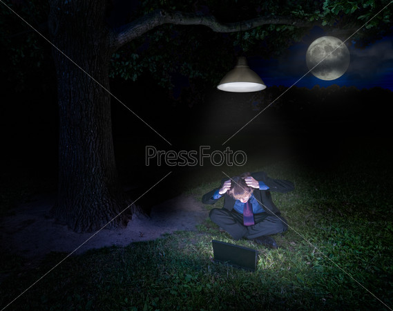 Frustrated young man with laptop in forest under the lamp at night