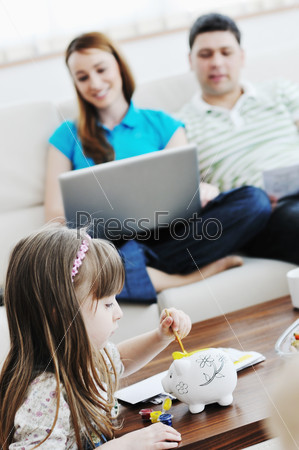 young happy family at bright and modern living room puting money in piggy bank and working on laptop computer on home finance