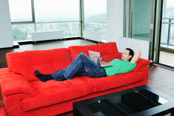 young man relax on red sofa and work on laptop at home indoor
