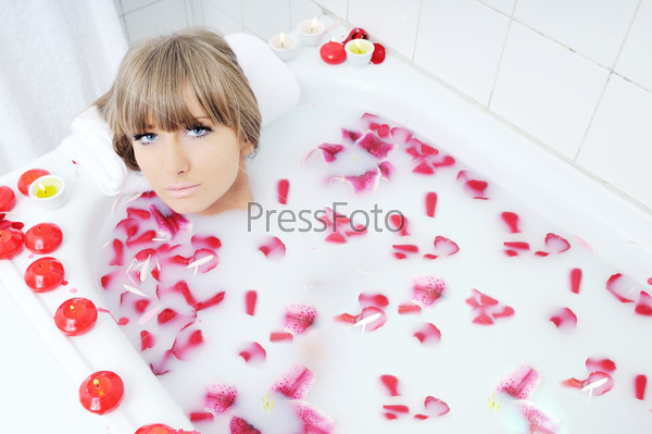 woman beauty spa and wellness treathment with red flower petals in bath with milk