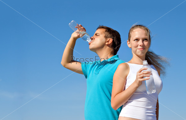 young couple with bottles of water against blue sky