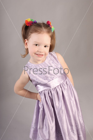 The small lovely girl in violet dress on gray background