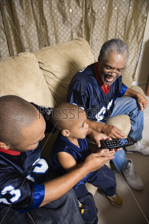 Three male generations of an African-American family watching football game on tv with boy holding remote.