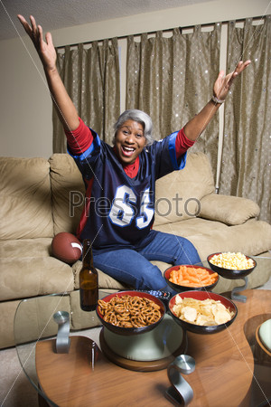 Portrait of a Middle-aged African-American woman wearing a football jersey with hands in the air watching football game.