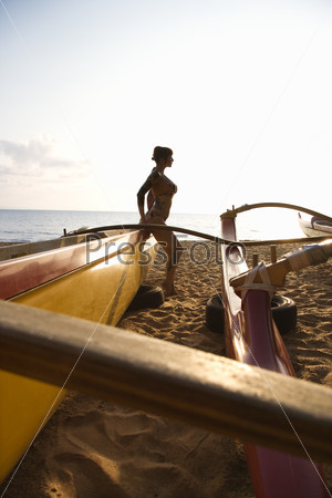 Silhouette of sexy Caucasian woman in bikini beside outrigger canoe on beach in Maui, Hawaii, USA.