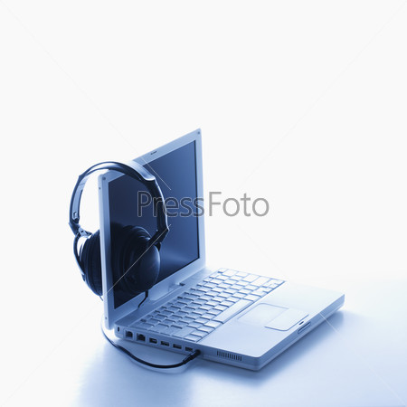 A pair of black headphones connected to a laptop and hanging on the screen. Square format. Isolated on white.