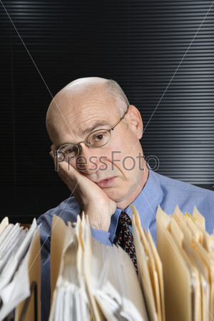 Caucasian middle-aged businessman with files leaning head on hand looking tired.