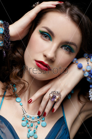portrait of young beautiful brunette woman in jewelry on black touching her face