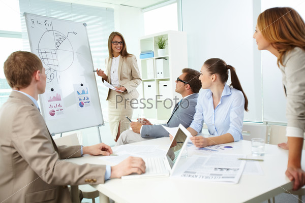 Confident top manager standing by the whiteboard and explaining her strategy at meeting