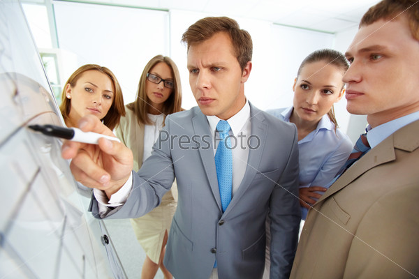 Serious boss pointing at whiteboard surrounded by his colleagues