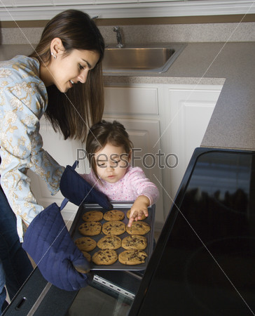 Caucasian mother and daughter  taking cookies out of oven.