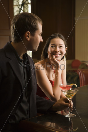 Taiwanese mid adult woman and Caucasian man standing at bar with drinks.