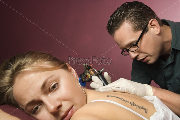 Caucasian male tattoo artist tattooing Caucasian woman.