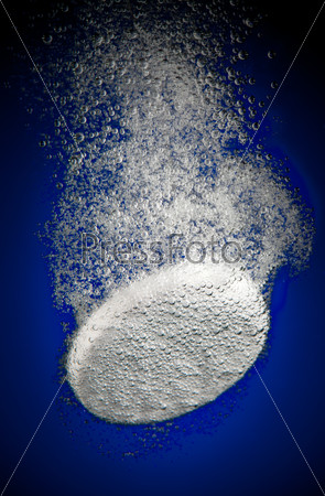 Effervescent tablet in water with bubbles on a blue background