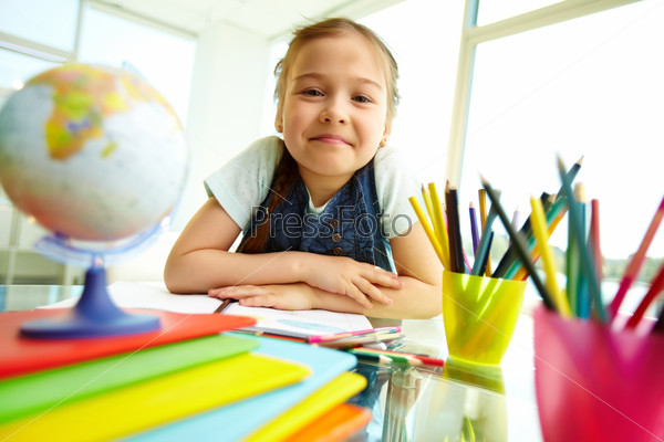 Portrait of lovely girl looking at camera with colorful pencils near by