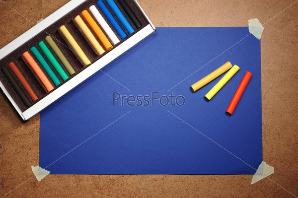 Empty blue cardboard background and multicolored pastel - art utensil