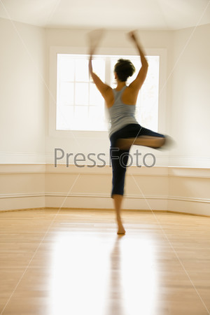 Young woman in motion jumping and dancing indoors by sunlit\
window.