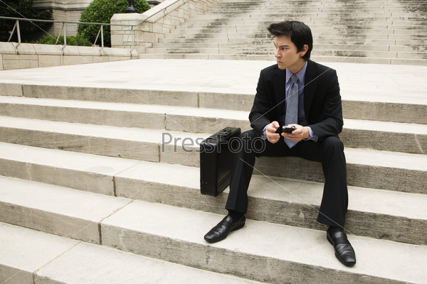Asian business man sitting on steps in urban area.