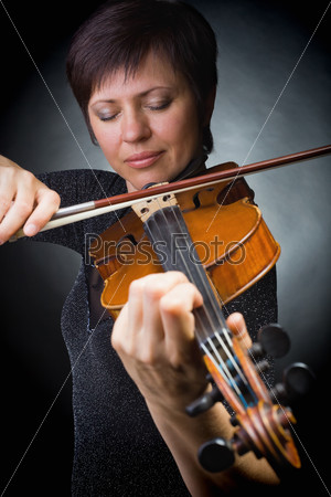 Beautiful woman playing the violin on dark background