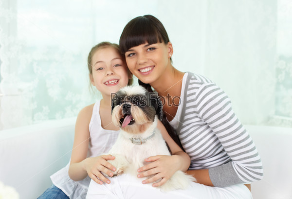 Portrait of happy girl and her mother holding pet and looking at camera with smiles