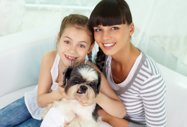 Portrait of happy girl and her mother holding pet and looking at camera