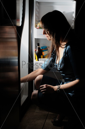 young woman in a dress looking inside of fridge
